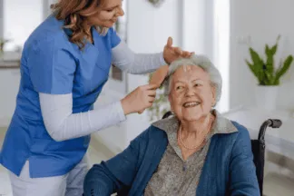 Smiling senior receiving grooming assistance from a caregiver, reflecting personal and daily living assistance and elderly care services. {{brizy_dc_image_alt imageSrc=